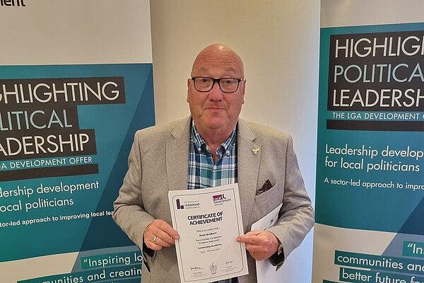 Robin Bradburn receiving a certificate of achievement in front of posters for a Leadership Development for Local Politicians training course