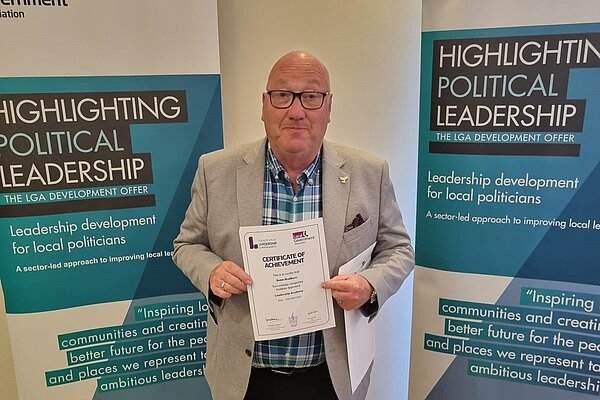 Robin Bradburn receiving a certificate of achievement in front of posters for a Leadership Development for Local Politicians training course